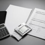 Smartphone haut de gamme posé près de documents de financement vierges et d’une calculatrice, dans une ambiance sobre de presse technologique.