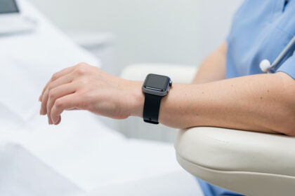 Gros plan réaliste d’une montre connectée portée au poignet d’une femme assise, le bras posé à hauteur du cœur dans un environnement clinique sobre.