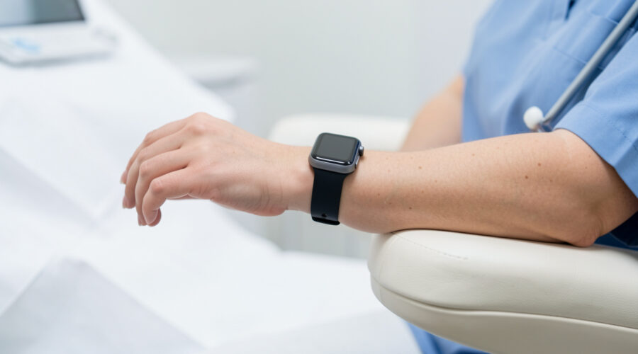 Gros plan réaliste d’une montre connectée portée au poignet d’une femme assise, le bras posé à hauteur du cœur dans un environnement clinique sobre.