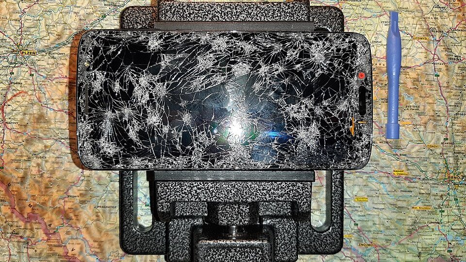 Téléphone à l'écran fracassé fixé dans un support de réparation, avec un outil d'ouverture en plastique